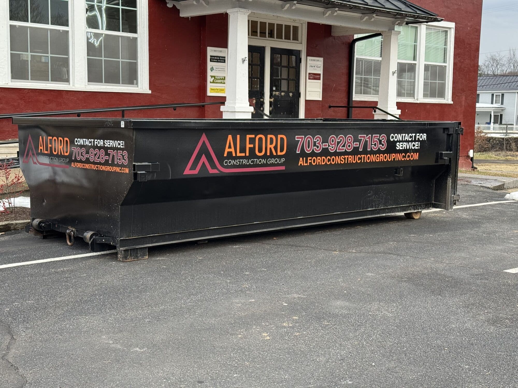An Alford Construction Group roll-off container parked outside a red brick building